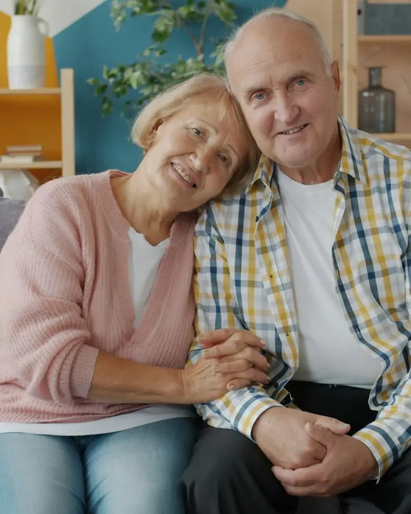 A silver-haired couple sitting close together on a sofa